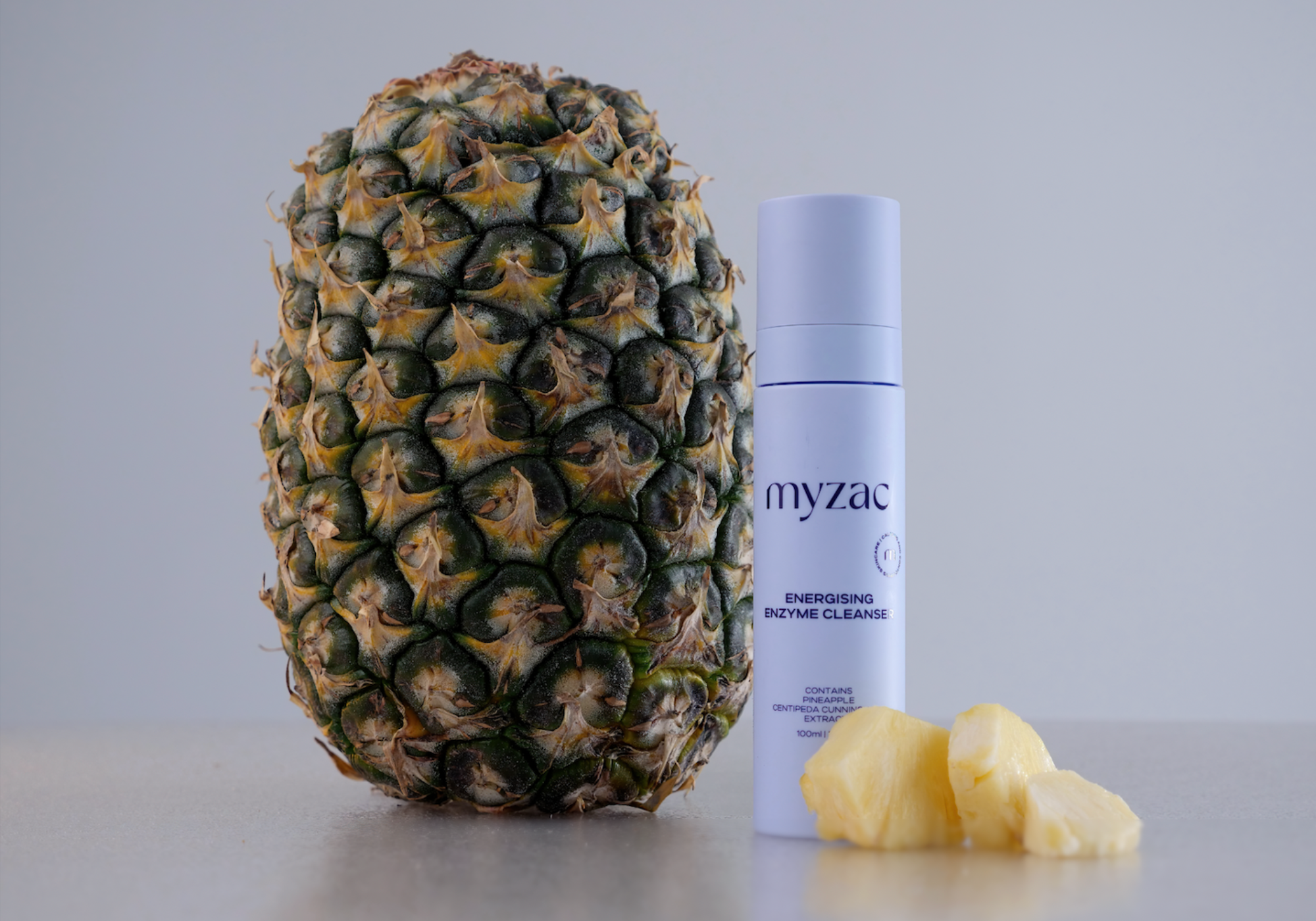 MYZAC Energising Enzyme Cleanser bottle with fresh pineapple, showcasing key natural ingredient.