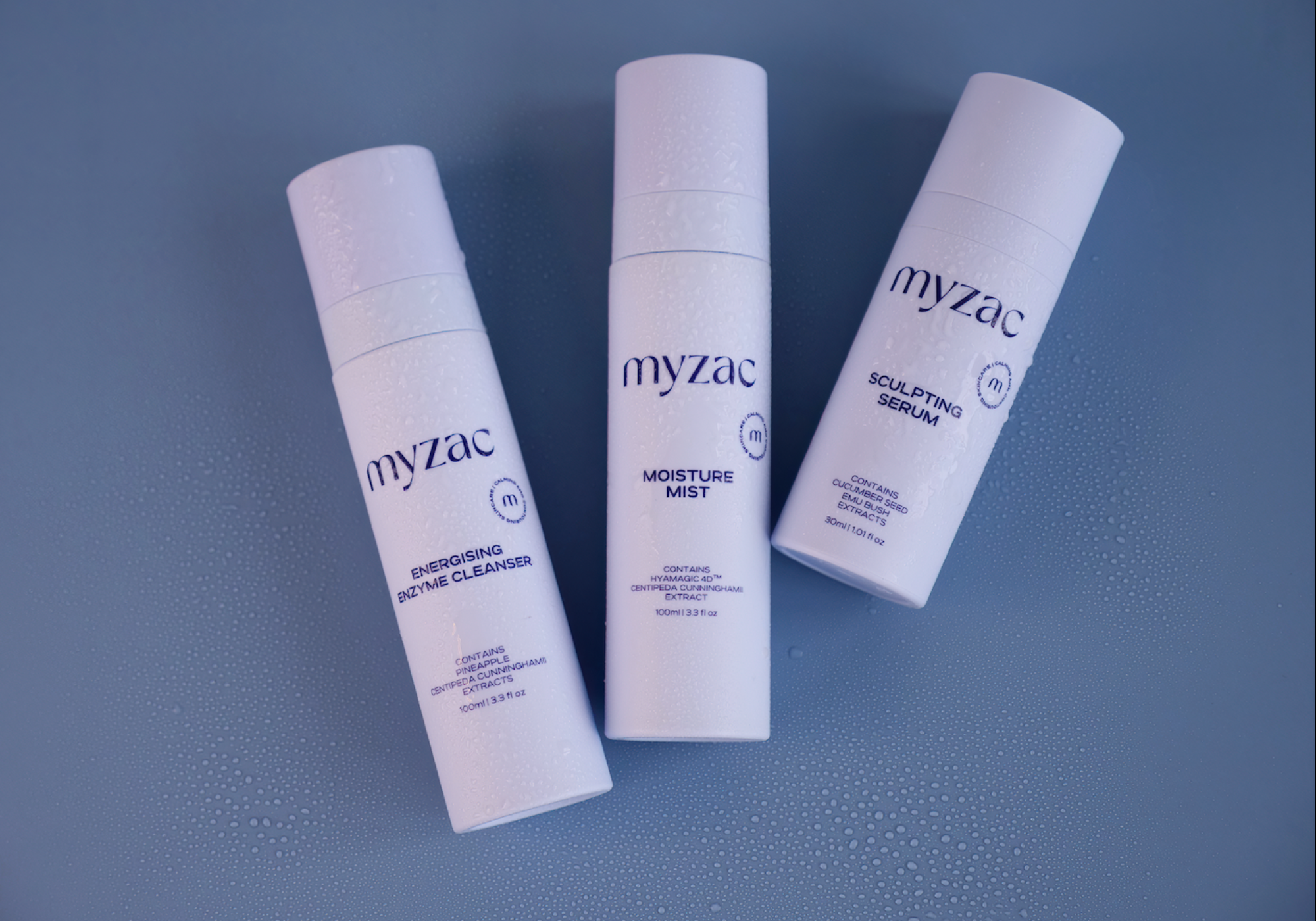 MYZAC Energising Enzyme Cleanser, Moisture Mist, and Sculpting Serum displayed together on a blue surface with water droplets, showcasing the complete skin recovery ritual.