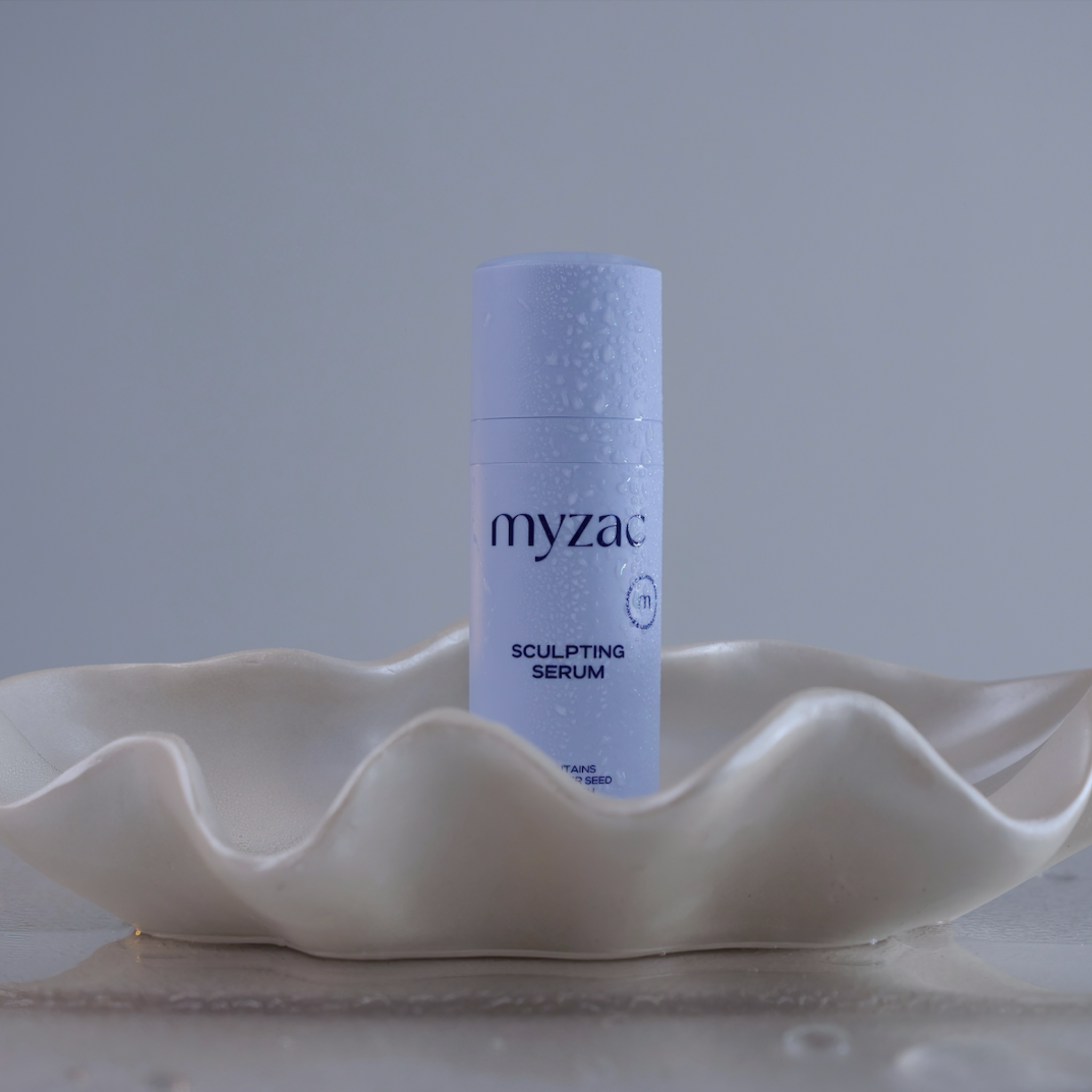 MYZAC Sculpting Serum bottle with water droplets, displayed in a shell dish for a premium spa-like feel.